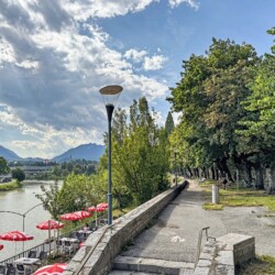 Draupromenade 12 Villach – riverside foot and cycle path along the Drau with a café terrace under red parasols
