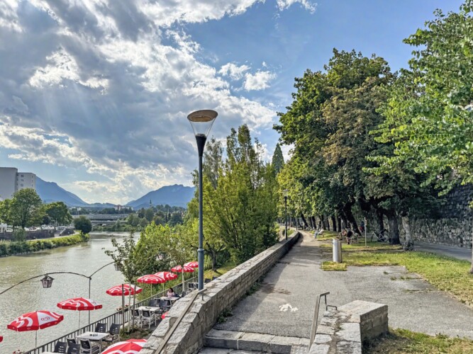 Draupromenade 12 Villach – riverside foot and cycle path along the Drau with a café terrace under red parasols