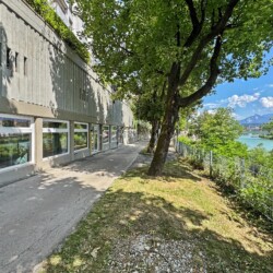 Draupromenade 12 Villach – ground-floor window front on the tree-lined riverside path beside the river Drau
