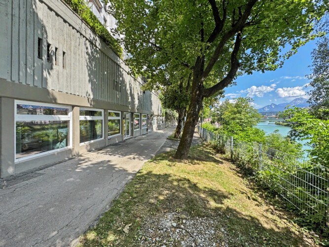 Draupromenade 12 Villach – ground-floor window front on the tree-lined riverside path beside the river Drau
