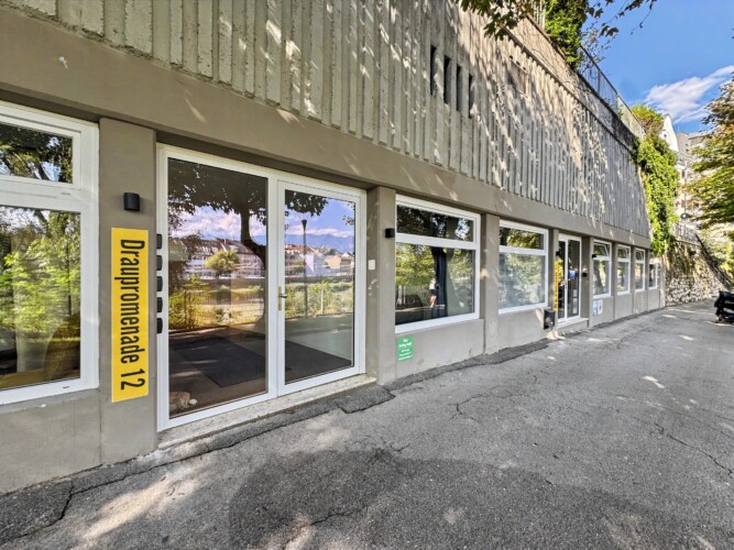 Draupromenade 12 Villach – building entrance with the yellow Draupromenade 12 sign and glass front door