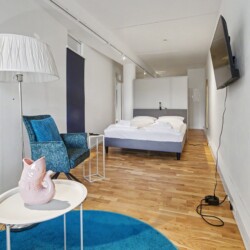 Draupromenade 12 Villach – Top 1 Türkis – open-plan living area with lounge corner, king bed and wall-mounted TV