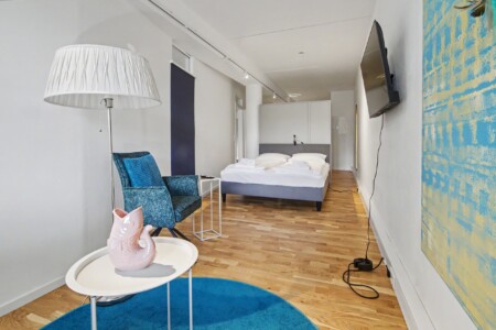 Draupromenade 12 Villach – Top 1 Türkis – open-plan living area with lounge corner, king bed and wall-mounted TV