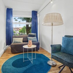 Draupromenade 12 Villach – Top 1 Türkis – lounge corner with grey sofa bed at the window and large blue-and-yellow painting