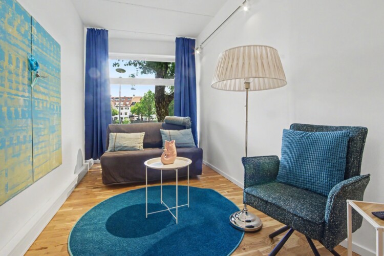Draupromenade 12 Villach – Top 1 Türkis – lounge corner with grey sofa bed at the window and large blue-and-yellow painting