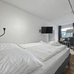 Draupromenade 12 Villach – Top 1 Türkis – king bed with upholstered headboard, black reading lamp and wall-mounted TV