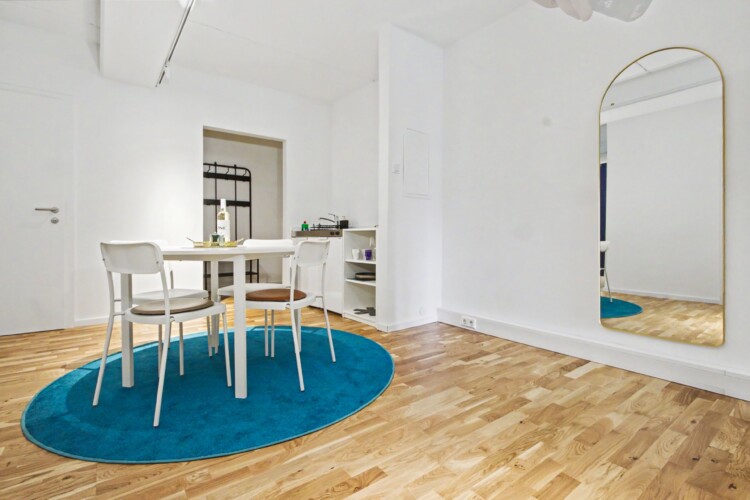 Draupromenade 12 Villach – Top 1 Türkis – round dining table with four chairs and full-length arched brass mirror
