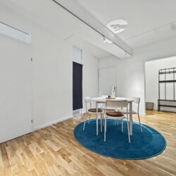 Draupromenade 12 Türkis Villach – Top 1 Türkis – dining table on the round rug with entrance hall and black coat rack behind