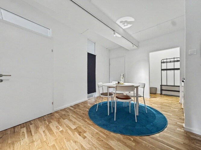 Draupromenade 12 Türkis Villach – Top 1 Türkis – dining table on the round rug with entrance hall and black coat rack behind