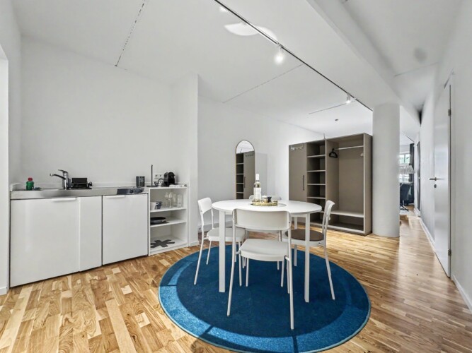 Draupromenade 12 Villach – Top 1 Türkis – kitchenette with sink and two hobs, round dining table and open wardrobe with hanging rail
