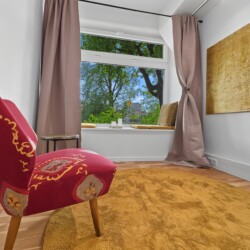 Draupromenade 12 Villach – Top 2 Gold – red vintage armchair beside the padded window seat, gold painting on the wall