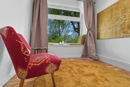 Draupromenade 12 Villach – Top 2 Gold – red vintage armchair beside the padded window seat, gold painting on the wall
