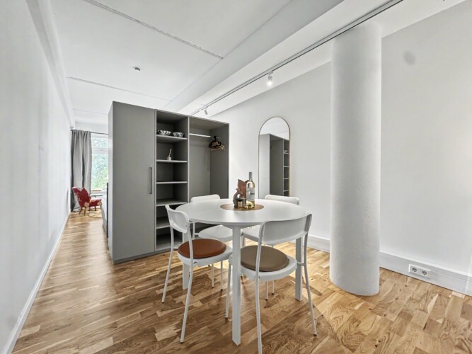 Draupromenade 12 Villach – Top 2 Gold – open-plan room with round dining table, exposed concrete column and open wardrobe
