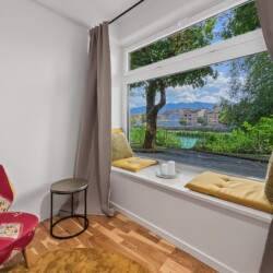Draupromenade 12 Villach – Top 2 Gold – padded window seat with mustard cushions and red armchair at the wide window