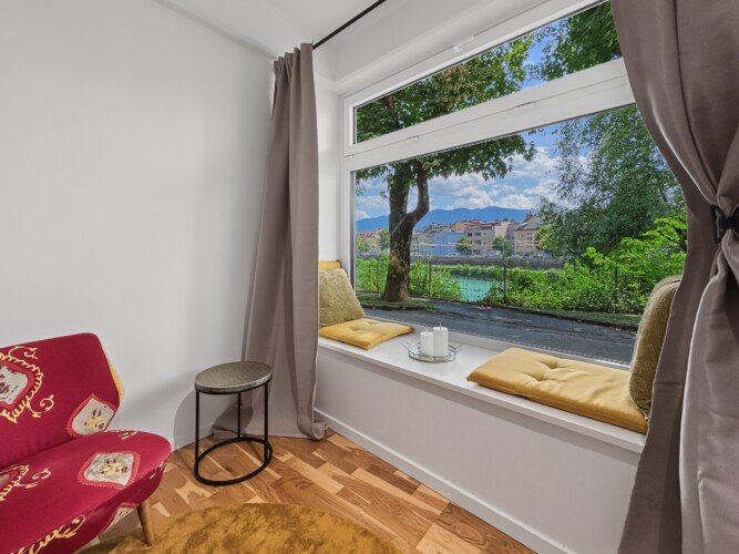 Draupromenade 12 Villach – Top 2 Gold – padded window seat with mustard cushions and red armchair at the wide window