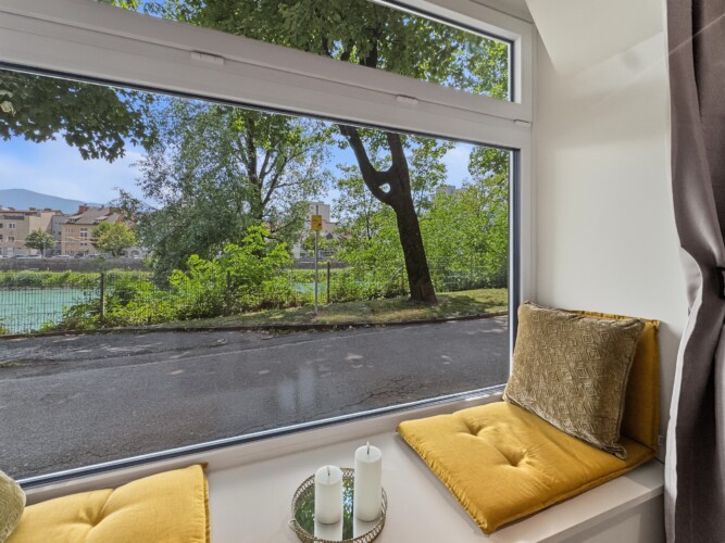 Draupromenade 12 Villach – Top 2 Gold – close-up of the padded window seat with mustard cushions and candles on the wide sill