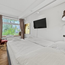 Draupromenade 12 Villach – Top 2 Gold – king bed with wall-mounted TV, gold painting and brass floor lamp