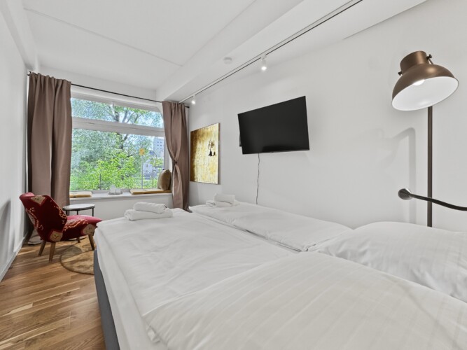 Draupromenade 12 Villach – Top 2 Gold – king bed with wall-mounted TV, gold painting and brass floor lamp