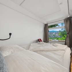 Draupromenade 12 Villach – Top 2 Gold – king bed made up with fresh towels, wall reading lamp and window seat beyond