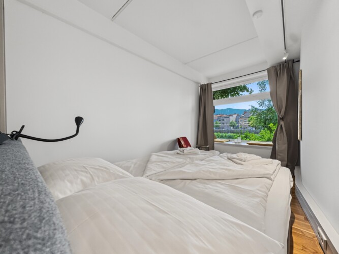 Draupromenade 12 Villach – Top 2 Gold – king bed made up with fresh towels, wall reading lamp and window seat beyond