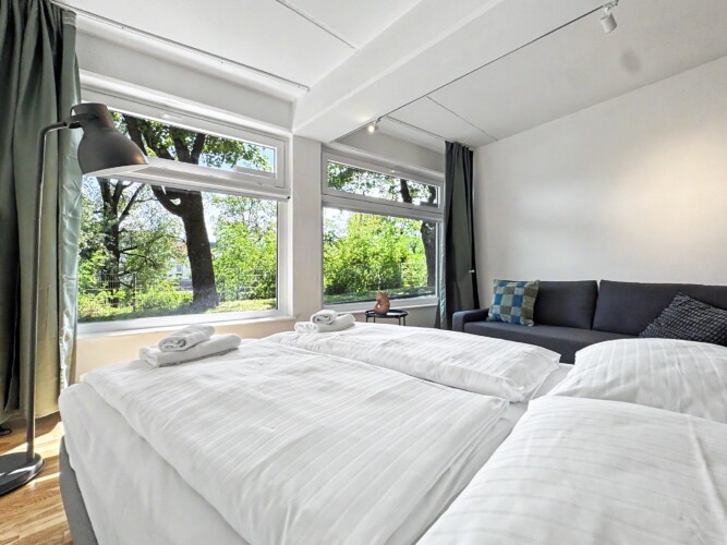 Draupromenade 12 Villach – Top 3 Drau – king bed made up with white linen and folded towels, sofa in the background