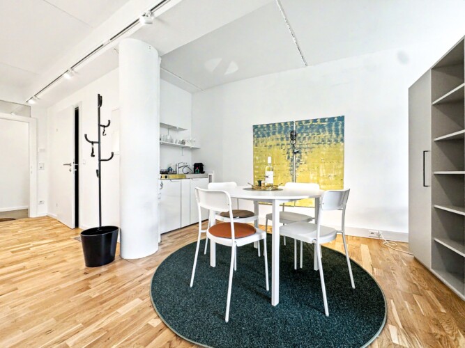 Draupromenade 12 Villach – Top 3 Drau – kitchenette with two hobs, sink, Nespresso machine and open shelf beside the round dining table