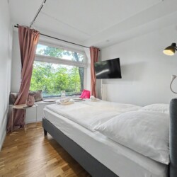 Draupromenade 12 Villach – Top 4 Pink – king bed with dusty-rose curtains, padded window nook and wall-mounted TV