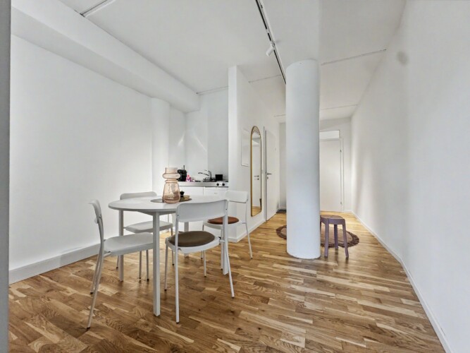 Draupromenade 12 Villach – Top 4 Pink – open living area with round dining table, oak parquet and round concrete column