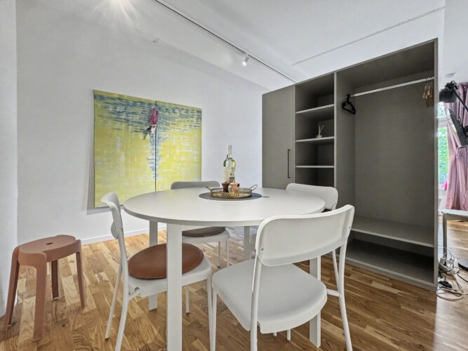 Draupromenade 12 Villach – Top 4 Pink – round dining table with four chairs beside the open built-in wardrobe with hanging rail