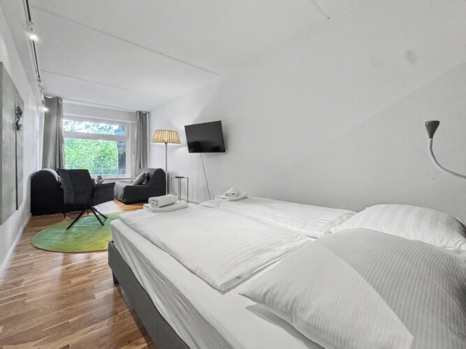 Draupromenade 12 Villach – Top 5 Grasgrün – open room with king bed, wall-mounted TV and lounge corner beyond