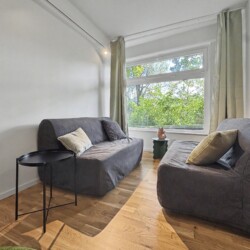 Draupromenade 12 Villach – Top 5 Grasgrün – two grey fold-out sofas facing each other at the window with sage-green curtains