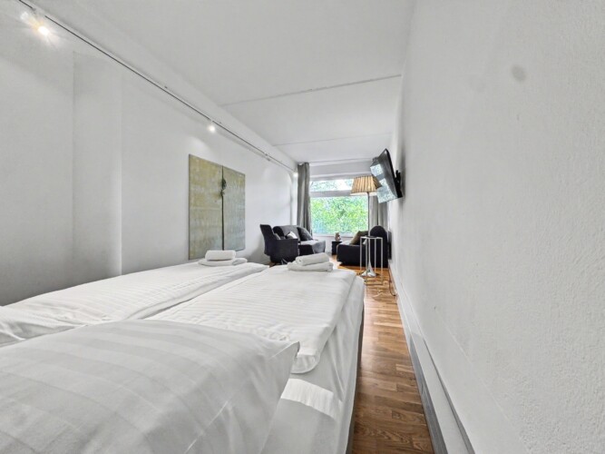 Draupromenade 12 Villach – Top 5 Grasgrün – king bed made up with white linen and rolled towels, artwork on the wall