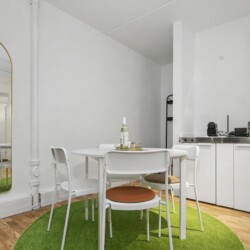 Draupromenade 12 Villach – Top 5 Grasgrün – round dining table with four chairs, kitchenette with two hobs and Nespresso machine, arched full-length mirror