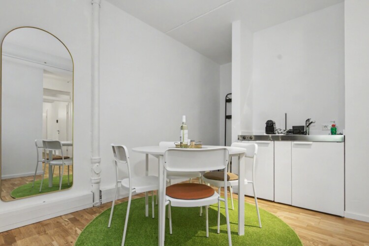 Draupromenade 12 Villach – Top 5 Grasgrün – round dining table with four chairs, kitchenette with two hobs and Nespresso machine, arched full-length mirror