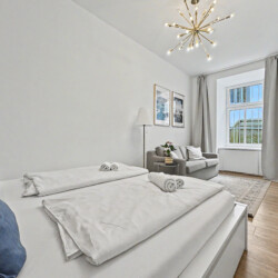 Bright living room with grey sofa, golden accents and high ceilings in Vienna Altbau apartment for 2 guests