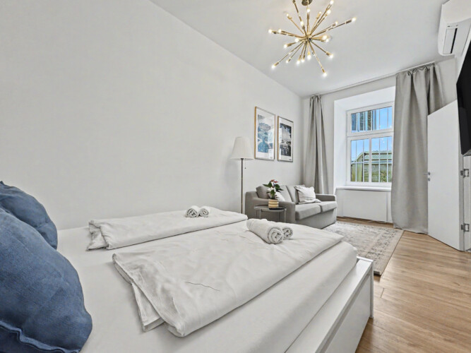 Bright living room with grey sofa, golden accents and high ceilings in Vienna Altbau apartment for 2 guests